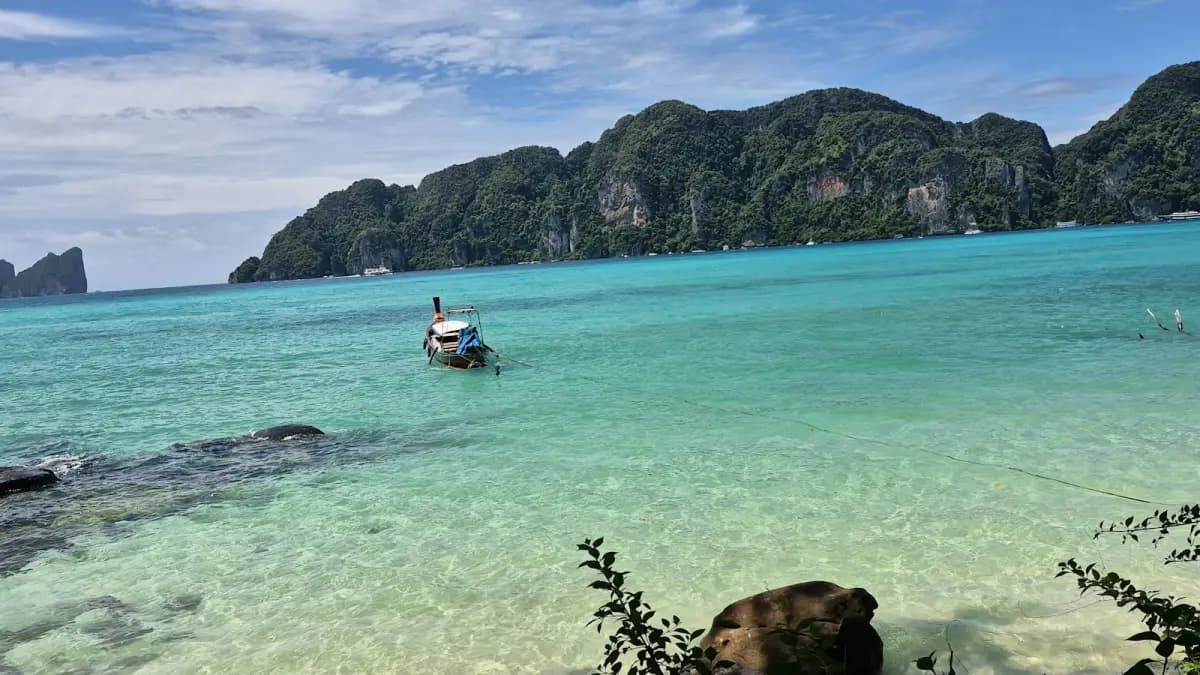 Long-tail boat floating in clear turquoise water near limestone cliffs in Thailand